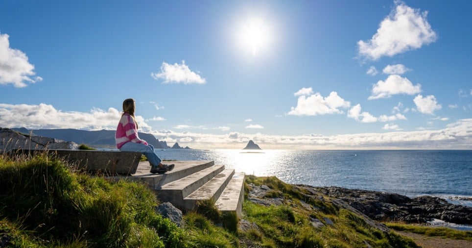 En kvinne som sitter på en trapp og ser ut mot horisonten over havet.