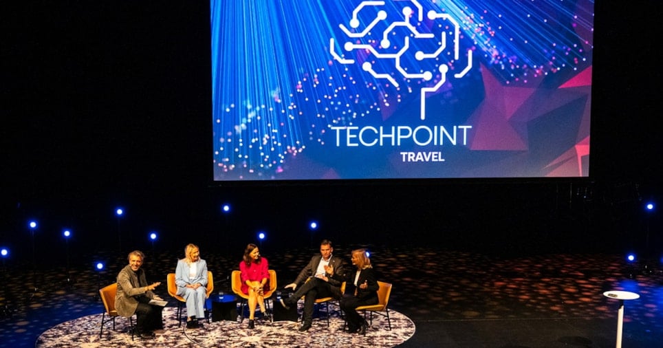 Fem personer som sitter på en scene med logoen til Techpoint Travel som viser