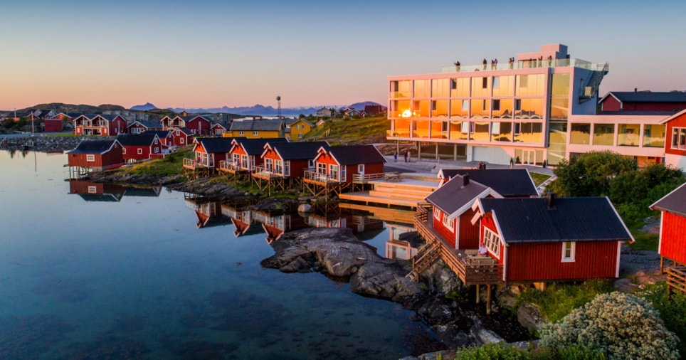 Mange røde trehus på rekke som står foran en bygning. Foto.