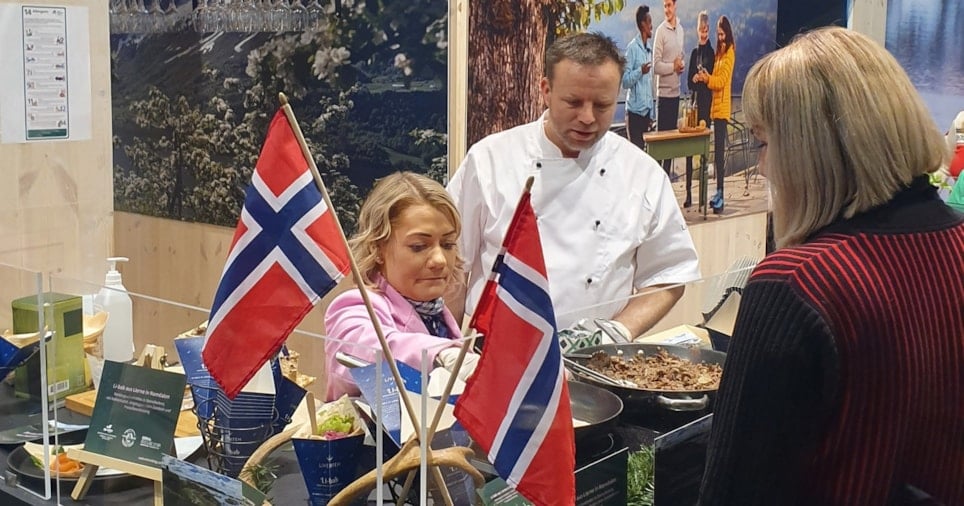 2 personer som står på bak en matstasjon og kokkelerer, men det norske flagget foran dem.