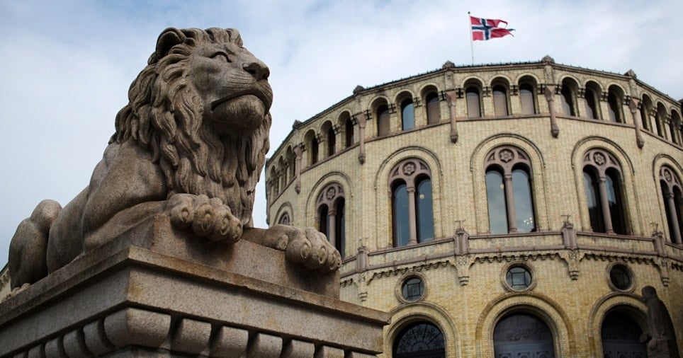 En løvestatue med Stortinget i bakgrunnen. Det norske flagget vaier fra toppen av Stortinget. Foto