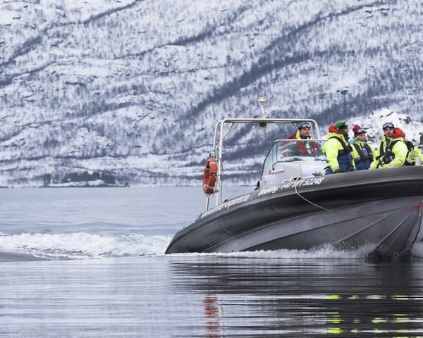 Mennesker i en båt med snødekkede fjell i bakgrunnen. Foto.