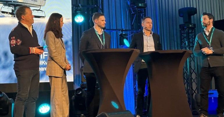 Fem personer som står på en scene under en panel debatt