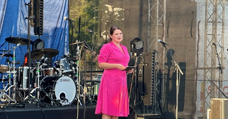En kvinne i rosa kjole som står på en scene. I bakgrunnen sees et trommesett. Foto