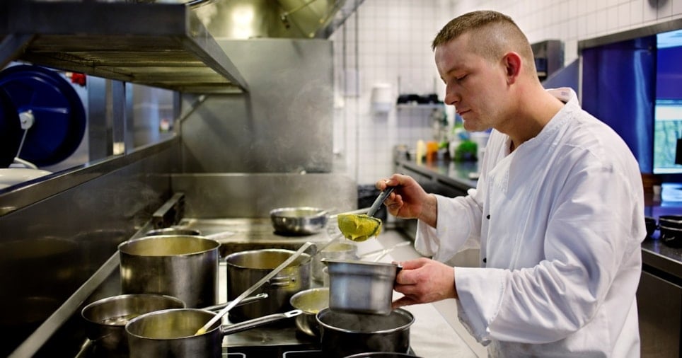 Mannlig kokk som rører i grytene på et restaurantkjøkken. Foto.