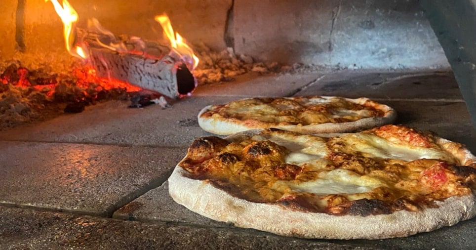 Stenovn med to pizzaer og flamme i bakgrunnen. Foto.