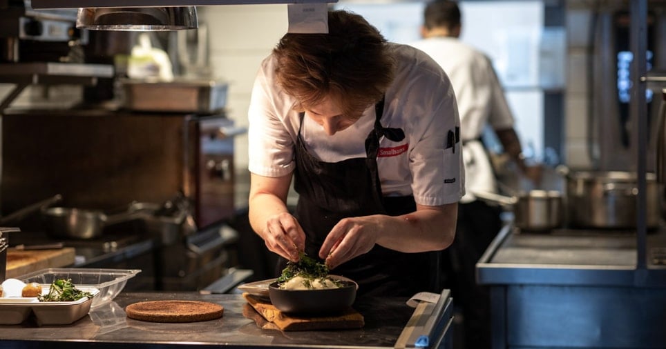 Ung kokk som legger garnityr på en tallerken, på et restaurantkjøkken. Foto.