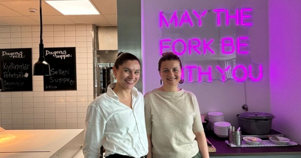 To damer foran kantine. Neonskilt i bakgrunnen hvor det står "may the fork be with you"